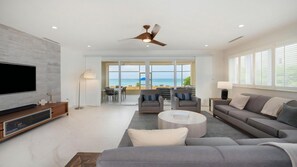 A modern living room with a flat-screen TV, grey sofas, a coffee table, and a ceiling fan.