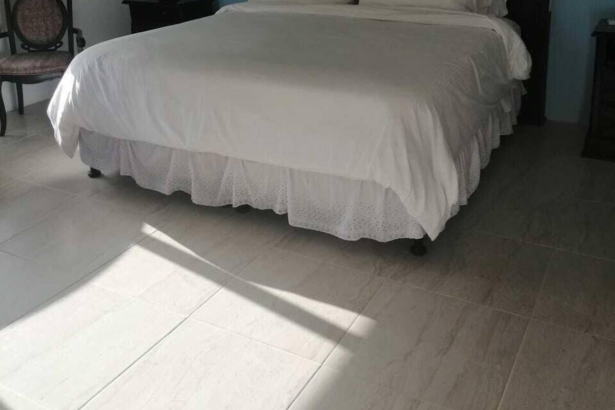 A neatly made bed with a white bedspread and pillows, a wooden headboard, and a nightstand with a lamp.