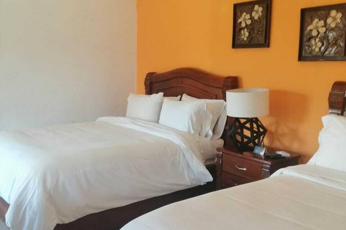 A hotel room with two beds, a nightstand with a lamp, and two wall-mounted air conditioning units.