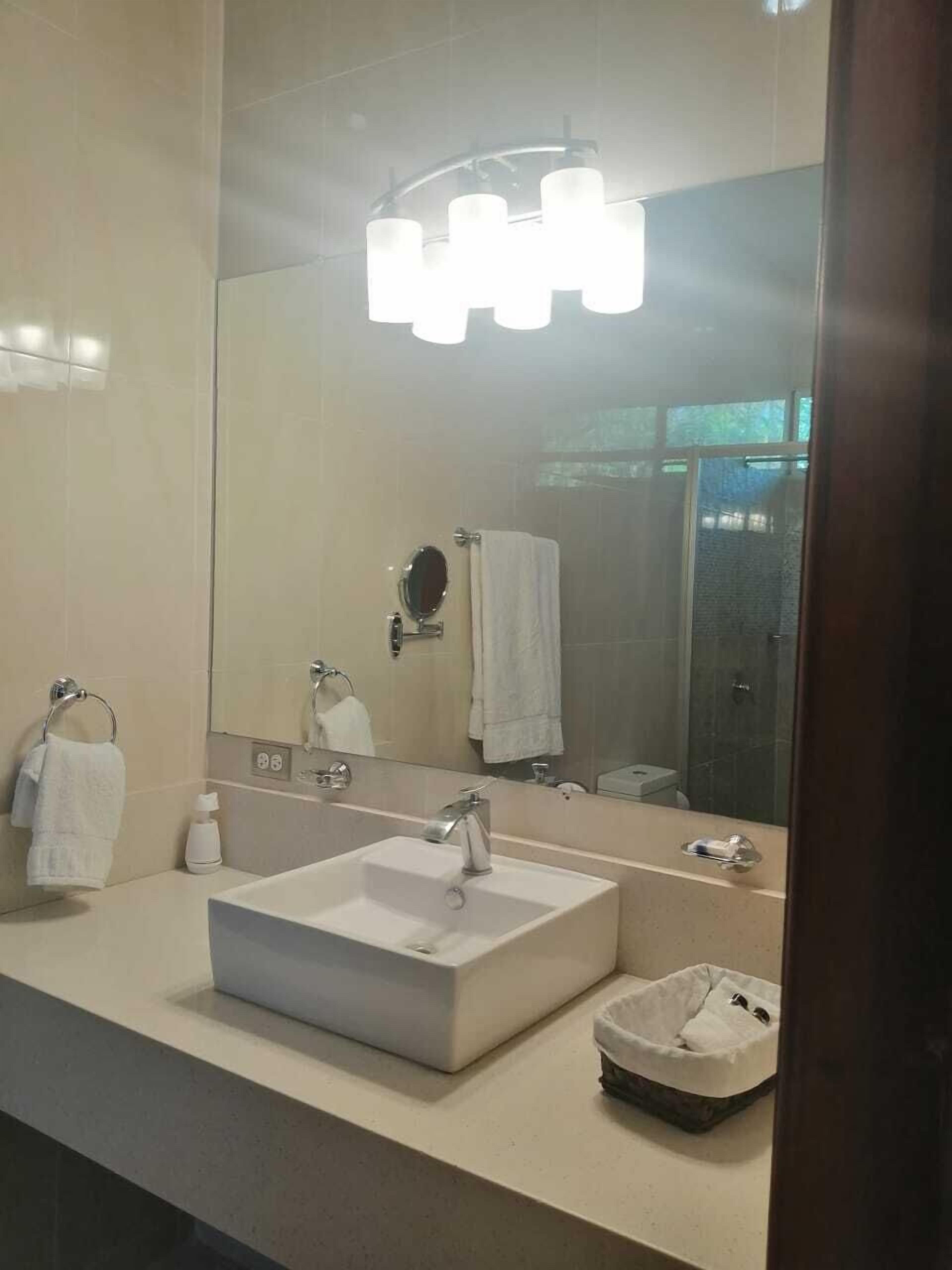 A modern bathroom with a large mirror, a white sink, and a shower area.