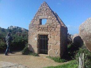 A stone structure with a triangular roof, a barred entrance, and a sign on the door.