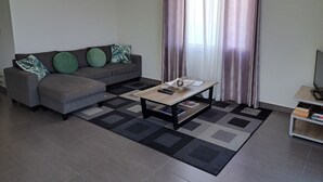 Ein Wohnzimmer mit grauem Sofa, einem Couchtisch und einer TV-Konsole.