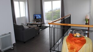 Ein modernes Wohnzimmer mit grauem Sofa, einem Fernseher und Blick auf einen Balkon.