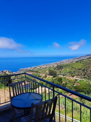 A balcony with a table and chairs overlooking a coastal landscape.