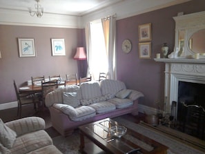 Een woonkamer met een bank, stoelen, een eettafel en een open haard.
