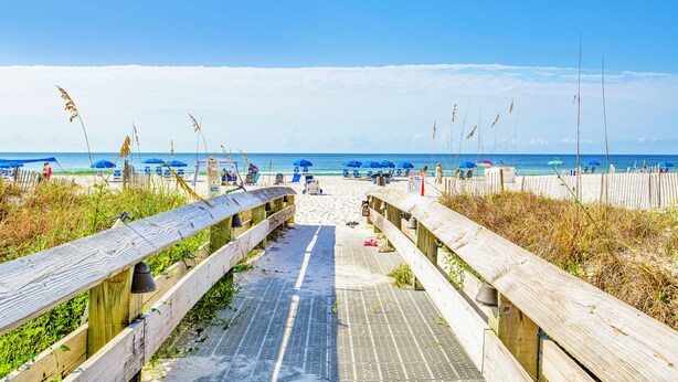 A wooden boardwalk leading to a beach with blue umbrellas and a clear sky. - Beachfront 1BR @ Phoenix IV • Sleeps 4 • Stunning Views, Balcony & Resort Amenities (Orange Beach)