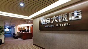 A hotel reception area with a reception desk, two staff members, and a sign indicating the hotel name. - Metro Hotel (Yunlin)