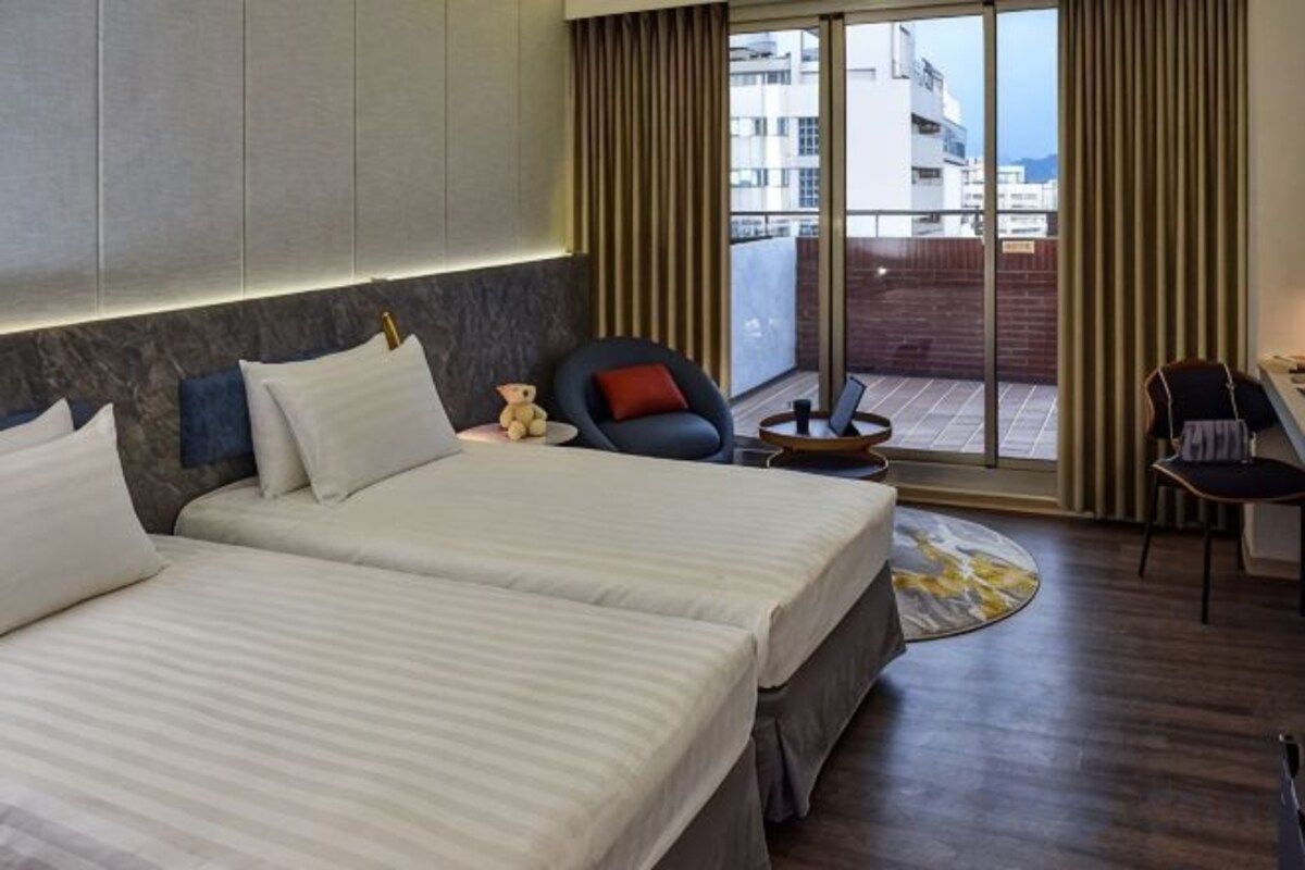 A hotel room with two beds, a balcony with a view, and a desk with a chair.