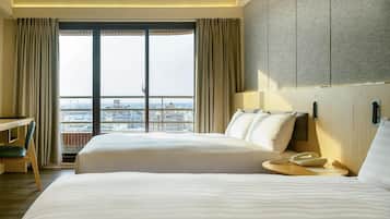 A hotel room with two beds, a desk, and a view of the city.