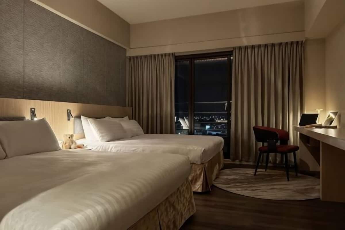 A hotel room with a large bed, a desk, and a view of the city at night.