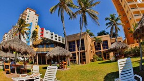 A resort with outdoor seating, palm trees, and modern buildings. - 2BR Beach Villa at Villas el Rancho / unit 5 (Mazatlán)