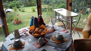A round table with a quilted tablecloth, a bowl of bread, a teapot, and a cup. - Room, Jacuzzi, Table d'hôtes on reservation (TREDUDER)