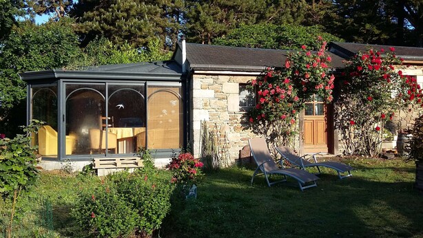 A stone house with a glass-enclosed porch, a wooden door, and a garden with red flowers. - Room, Jacuzzi, Table d'hôtes on reservation (TREDUDER)