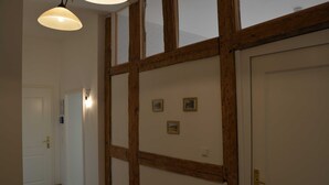 Un pasillo con techo de vigas de madera, una puerta blanca y una pared con tres cuadros pequeños enmarcados.