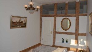 Un dormitorio con cama, candelabro, puerta, espejo y un cuadro en la pared.