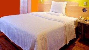 A hotel room with a bed, a bedside table with a telephone, and a wall-mounted light fixture. - 7days Inn Hotel (Xinzhou)
