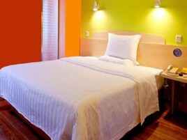 Una habitación de hotel con una cama, una mesita de noche con teléfono y una lámpara fijada a la pared.