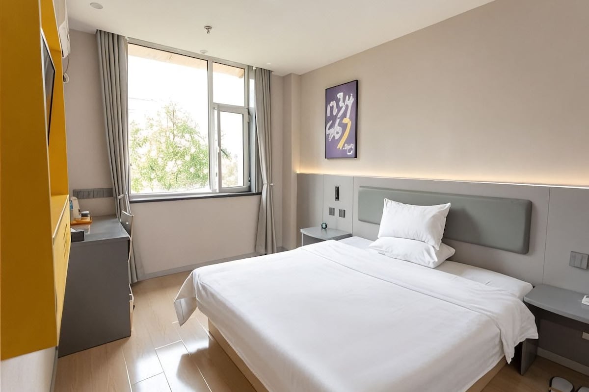 Ett modernt hotellrum med en stor säng, sängbord, ett skrivbord och ett fönster med gardiner.