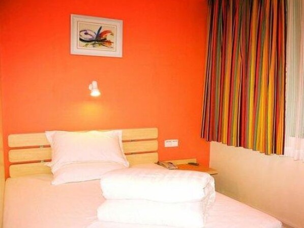 A hotel room with a bed, a wall-mounted light, a framed picture, and a window with colorful curtains.