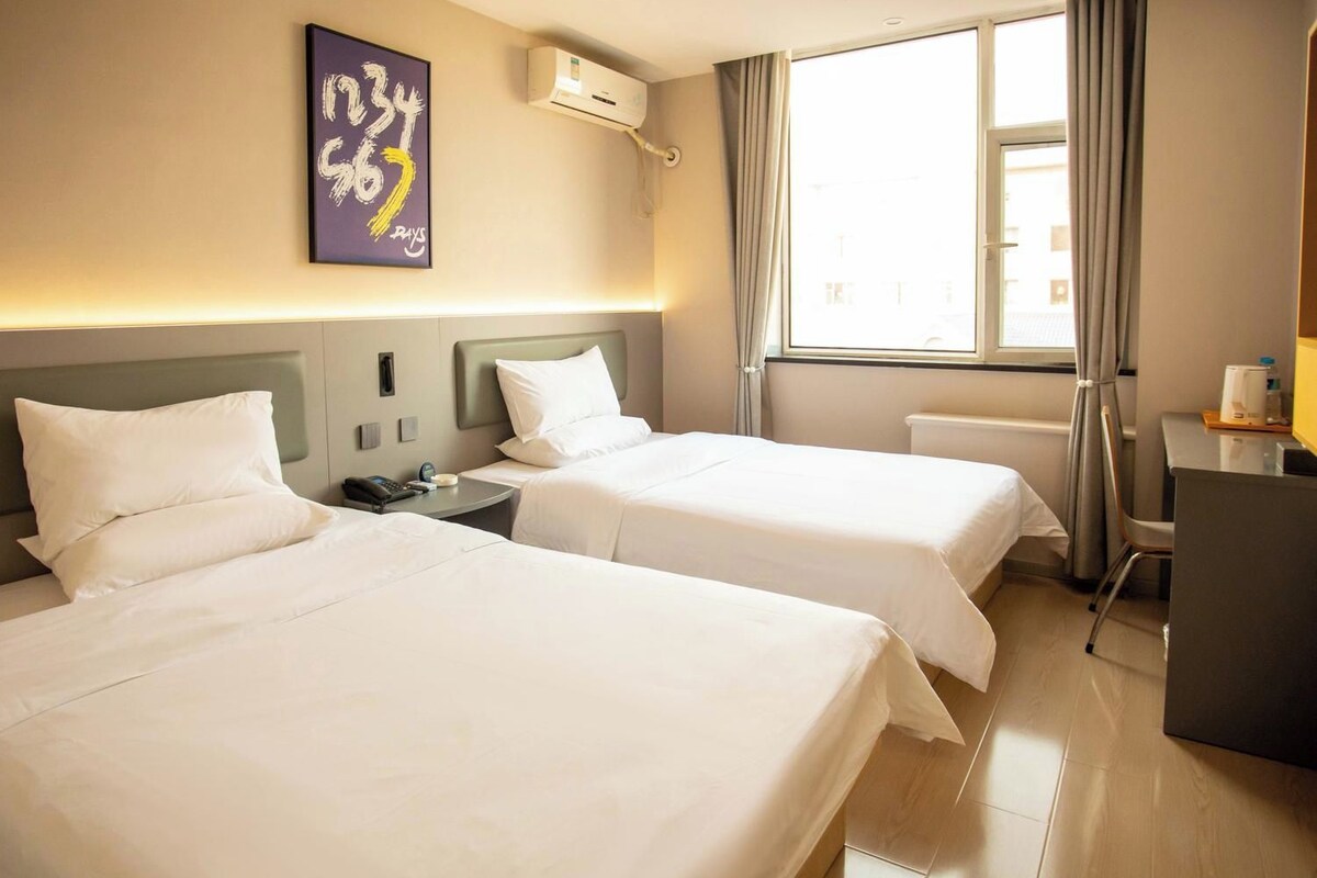 Ett hotellrum med två sängar, ett skrivbord, en luftkonditioneringsanläggning och ett fönster med gardiner.