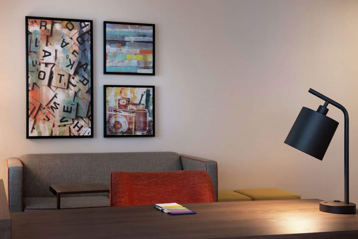Un salon moderne avec un canapé gris, un coussin rouge, une table basse en bois et un lampadaire noir. Trois œuvres d’art encadrées ornent le mur.