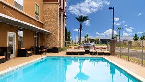 A swimming pool with lounge chairs and a building with stone and brick facade. - Hampton Inn & Suites Buena Park (Buena Park)