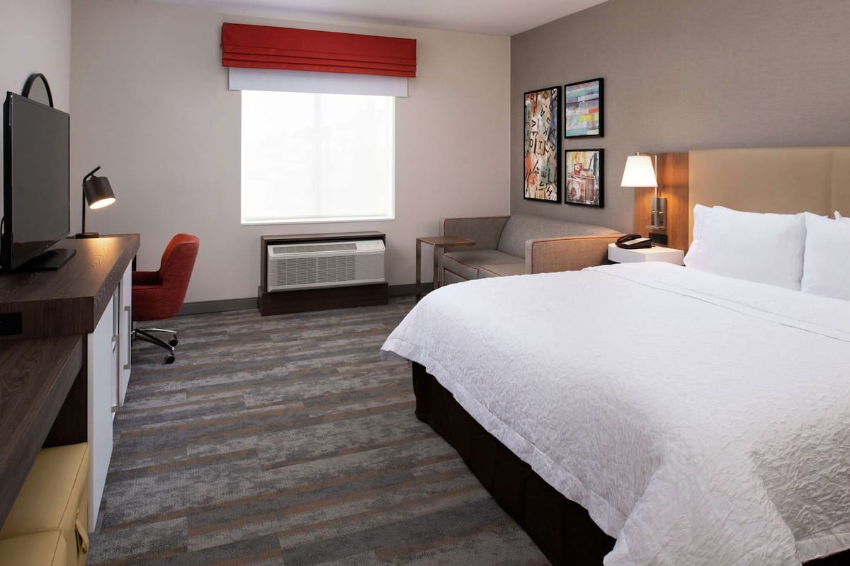 Une chambre d’hôtel avec un lit, un bureau équipé d’un ordinateur, une chaise, un radiateur et des œuvres d’art accrochées au mur.