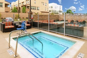Una piscina con cerramiento de vidrio, mobiliario exterior con cojines a rayas y un muro de ladrillo.
