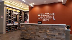 A reception desk with a wooden panel design, a 'Welcome to the Golden State' sign, and a shoe display area. - Hampton Inn & Suites Buena Park (Buena Park)
