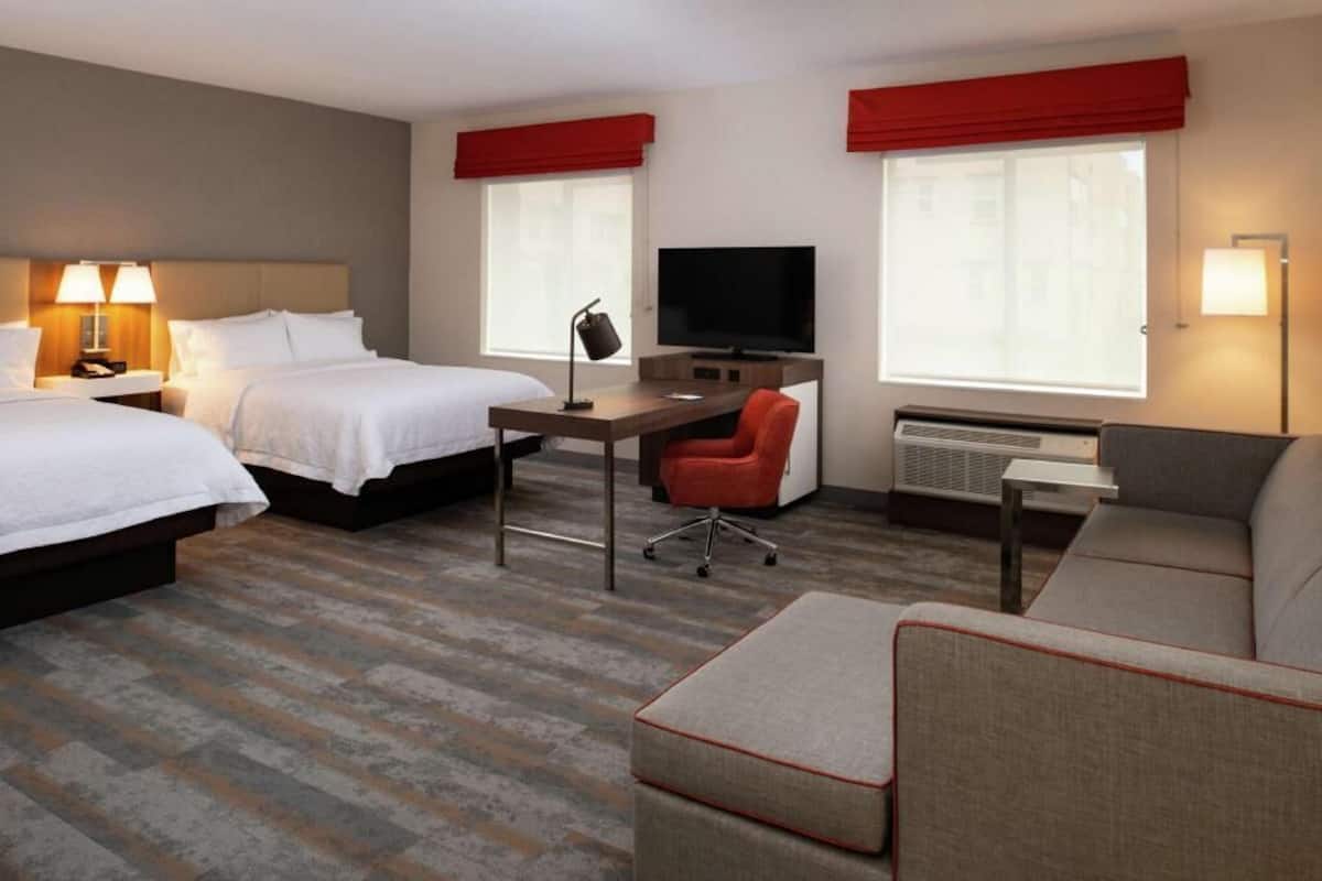 Une chambre d’hôtel avec deux lits, un bureau, une télévision, un canapé et un appareil de climatisation.