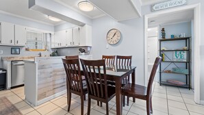 A kitchen with white cabinets, a wooden island, and a dining area with wooden chairs. - "Shore Beats Work" - 2nd Row Condo w/ Community Pool, 4 Bedrooms / 2 Bathrooms (Holden Beach)