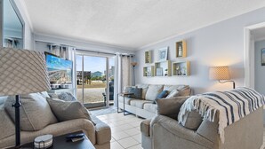 A living room with a sofa, armchair, lamp, and a remote control on a table. - "Shore Beats Work" - 2nd Row Condo w/ Community Pool, 4 Bedrooms / 2 Bathrooms (Holden Beach)