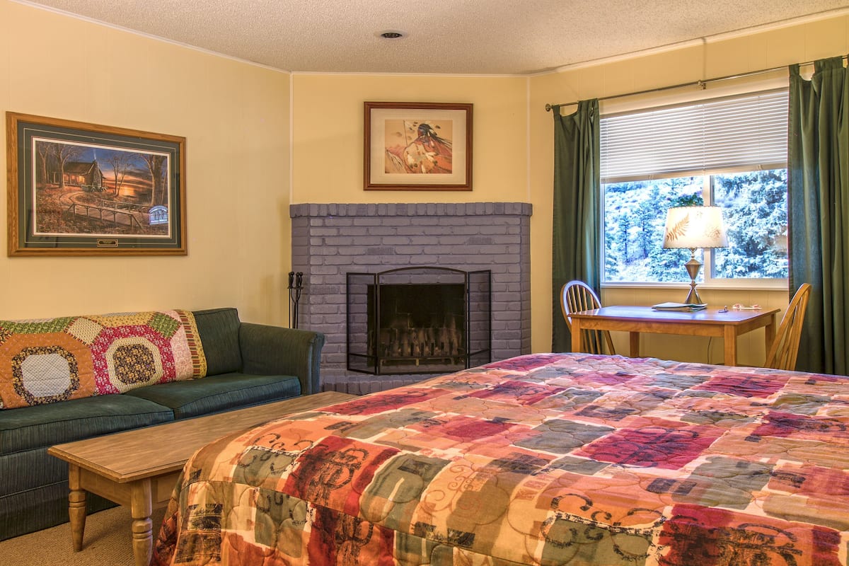 Una habitación acogedora con chimenea, una cama con colcha de colores, un sofá con un plaid estampado y un cuadro en la pared.