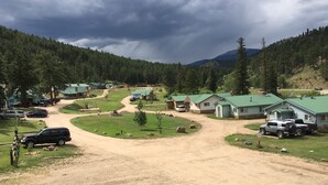 Un camping con varias cabañas, un camino de tierra y colinas boscosas circundantes.