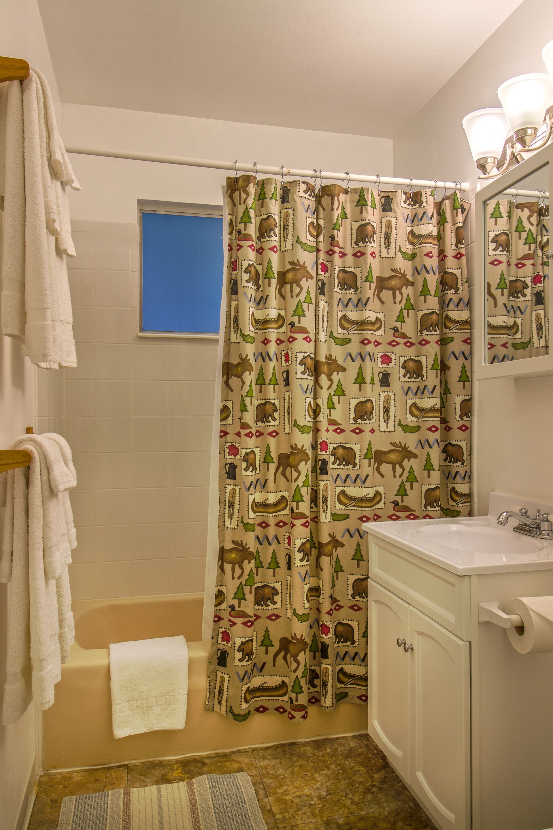 A bathroom with a shower curtain featuring a nature pattern, a bathtub, a sink, and a mirror.