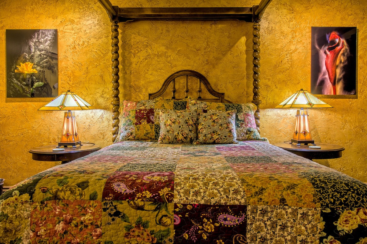 Una cama con colcha floral, dos lámparas de noche y dos cuadros en las paredes.