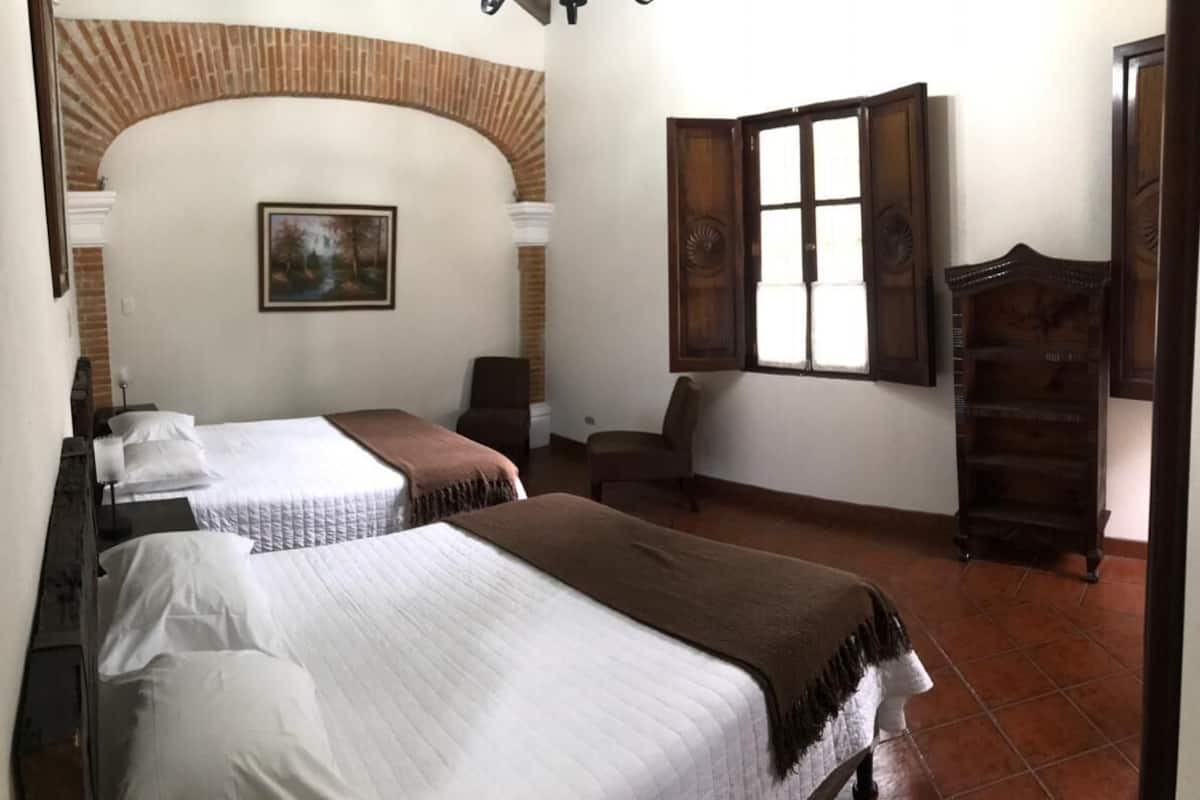 A room with two beds, a wooden cabinet, a chair, and a window with shutters.