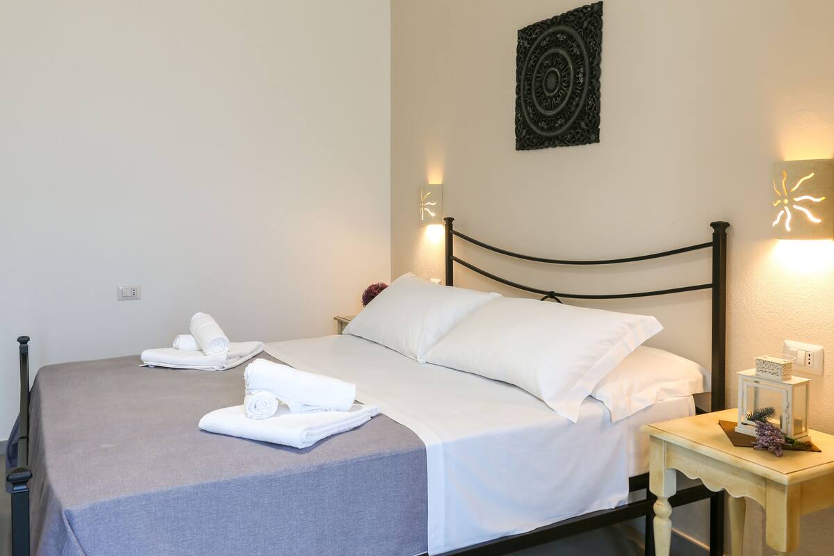 A neatly made bed with white linens, a bedside table with a lamp, and a wall-mounted decorative piece.