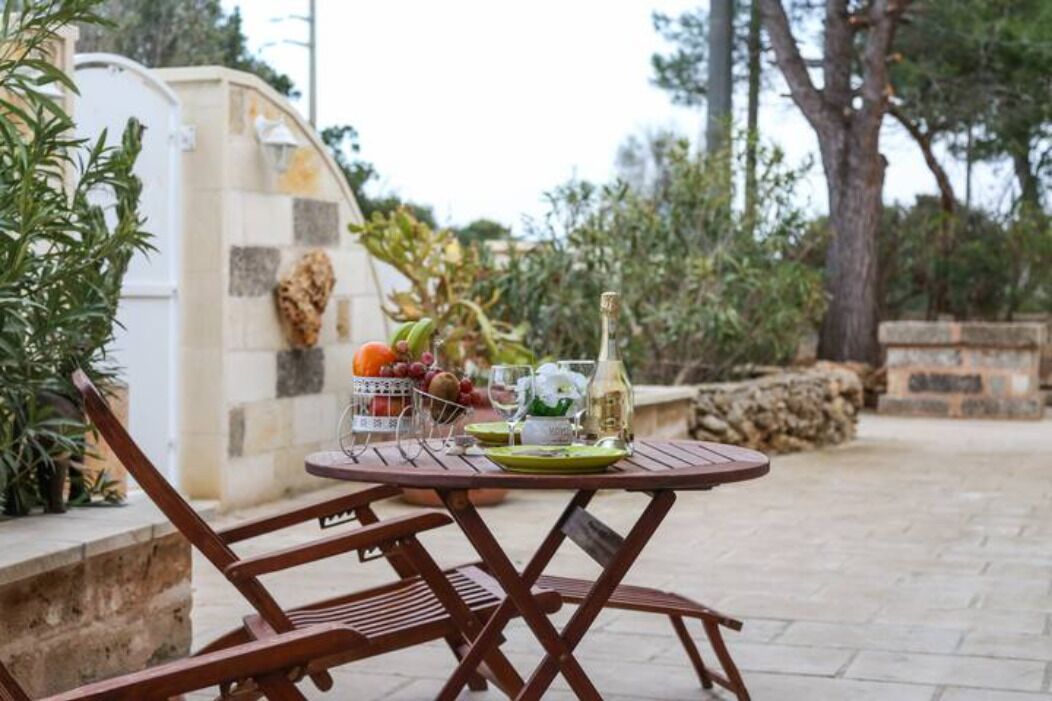 Un área de comedor al aire libre con una mesa redonda, una botella y una cesta de frutas.