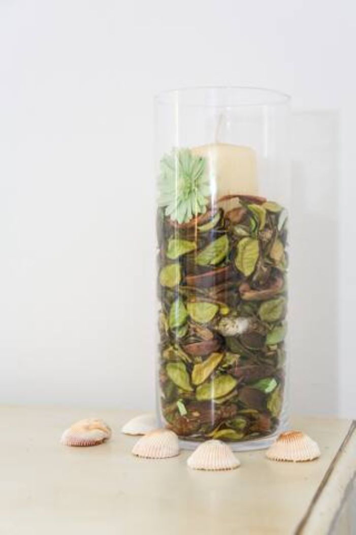 A clear glass container filled with various seashells and a candle.
