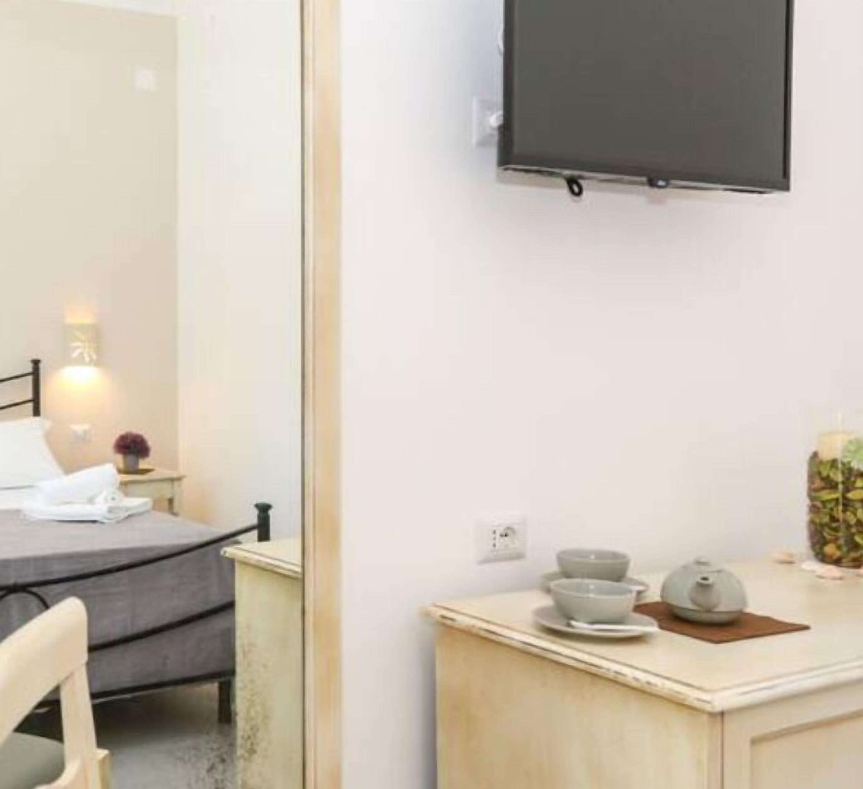 Une chambre d’hôtel comprenant un lit, une table de chevet avec un service à thé, un miroir et un téléviseur fixé au mur.
