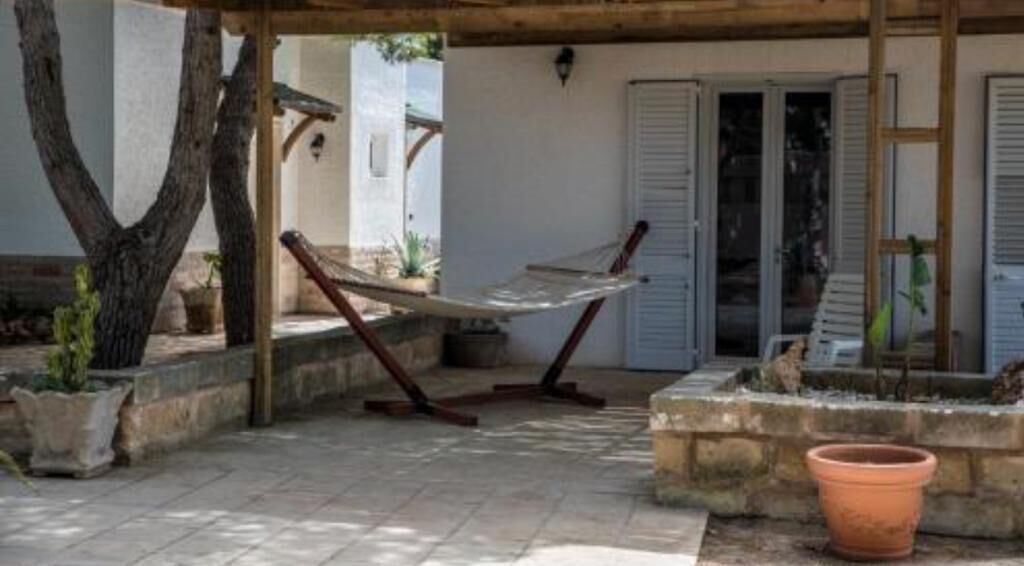 A covered outdoor area with a hammock, potted plants, and a door leading to a building.