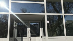 Entrada de un edificio con puerta de vidrio, un cartel y vistas a árboles y un cielo despejado.