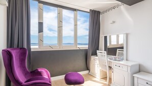 Una habitación con una silla morada, un tocador blanco y un amplio ventanal con vistas.