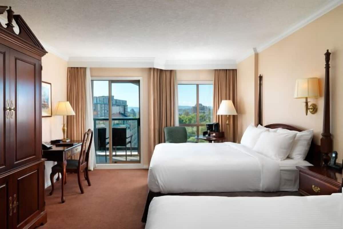 A hotel room with two beds, a desk, a chair, and a view of the city.