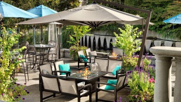 Eine Terrasse im Freien mit Tisch und Stühlen, umgeben von Pflanzen und Sonnenschirmen.