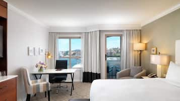 A hotel room with a bed, desk, chairs, and a view of the city.