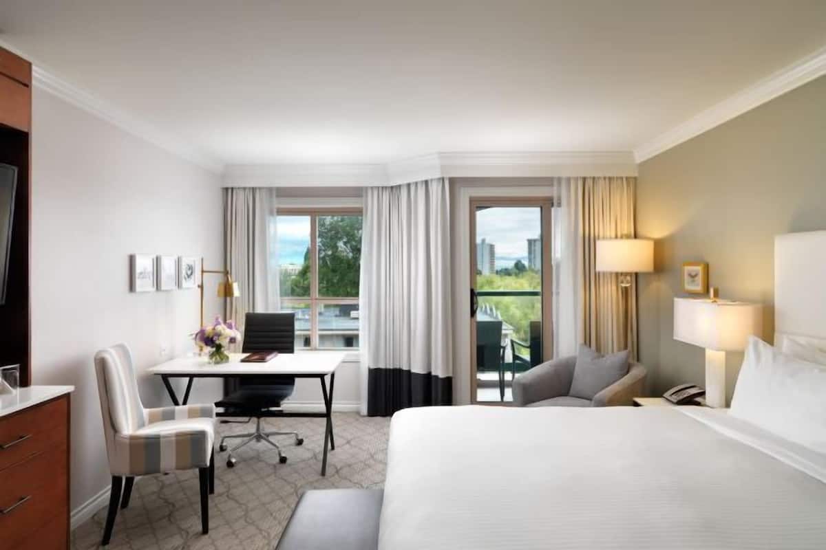 A hotel room with a bed, desk, chair, and a view of the outdoors.