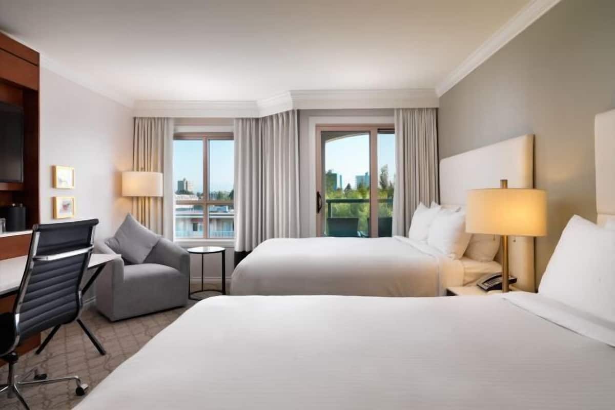 A hotel room with two beds, a desk, a chair, and a TV.