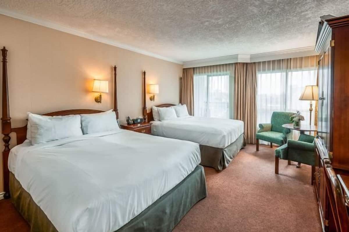 A hotel room with two beds, a green armchair, a small table, and a cabinet.